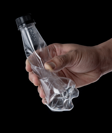 Hand holding empty used water bottle for recycling over dark background