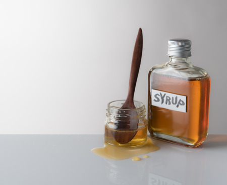 Glass bottle of syrup with spoon on gray background