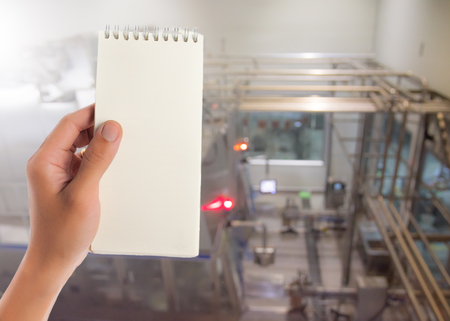 Hand hold blank notepad with space for text,Manufacturing factory blurredの写真素材