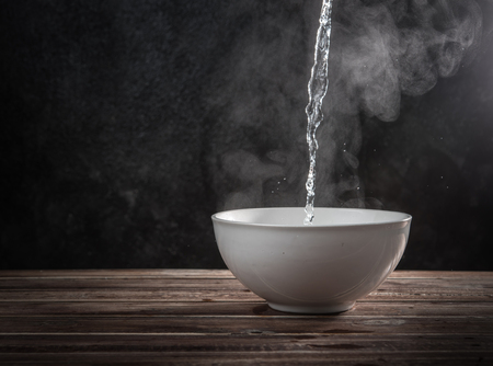 Pouring hot water into into a ceramic bowl against black cement wallの写真素材