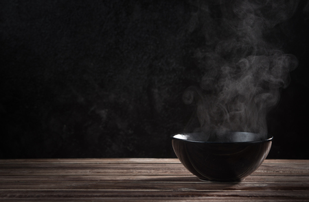 Steam of hot soup with smoke in ceramic bowl against black cement wallの写真素材