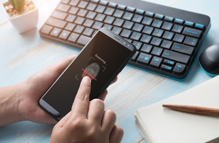 Hand holding smartphone with process of scanning fingerprint at office desk,unlock mobile phoneの写真素材