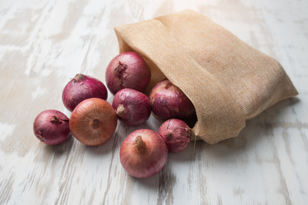 Red onion in sack on white wooden backgroundの写真素材