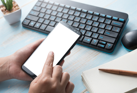Hands holding blank screen smartphone at office deskの写真素材