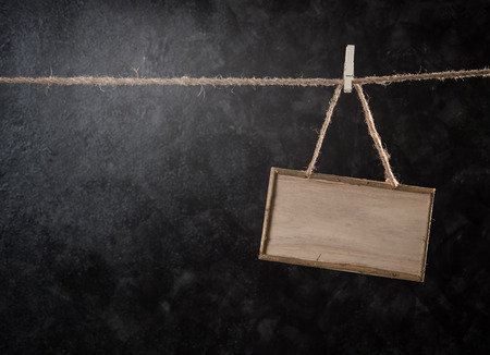 Wooden signboard hanging on rope against dark backgroundの写真素材