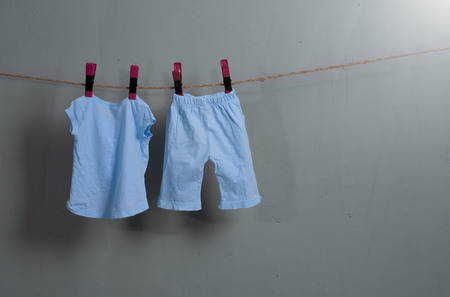 Baby clothes hanging on the clothesline against gray wall