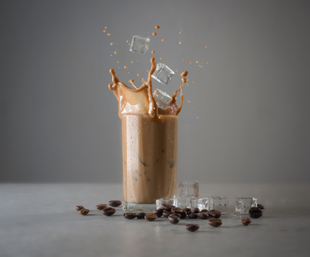 Iced coffee splash with ice cubes and beans against grey concreteの写真素材