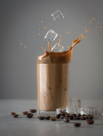 Iced coffee splash with ice cubes and beans against grey concreteの写真素材