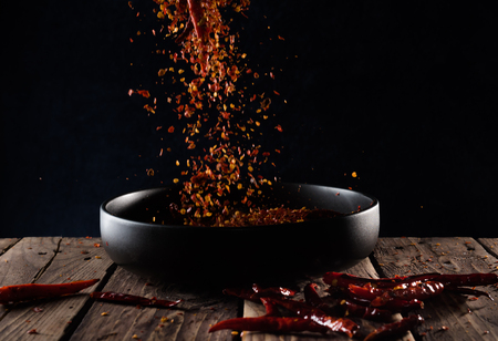 Pouring cayenne pepper powder into the bowl on wood table,Motion blurの写真素材