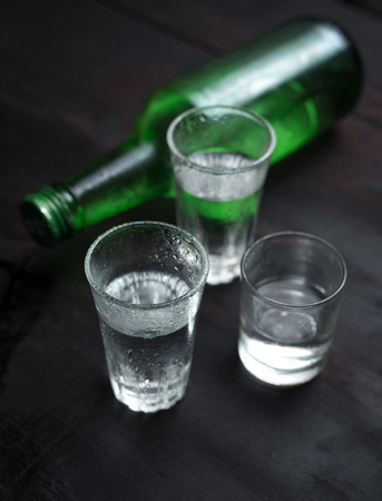 Alcoholic clear distilled korean Soju bottle with shot glass on a wooden background.の写真素材