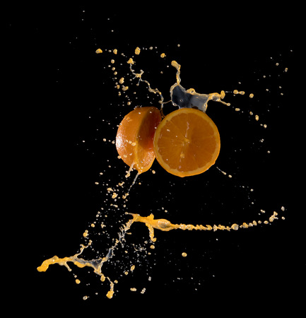 Fresh oranges with orange juice splashing isolated on blackの写真素材