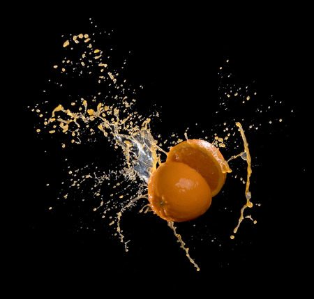 Fresh oranges with orange juice splashing isolated on blackの写真素材