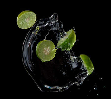 Limes with water splash or explosion flying in the air isolated on black backgroundの写真素材