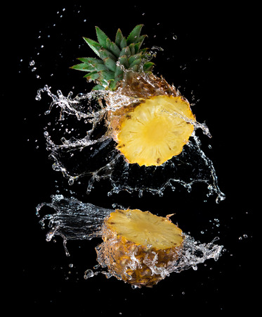 Slice of yellow pineapple with water splashing isolated on black backgroundの写真素材