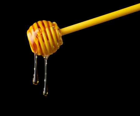 Honey dripping from plastic dipper on blackの写真素材