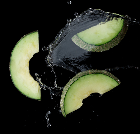Japanese melon green with water splash or explosion flying in the air isolated on blackの写真素材