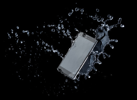 Smartphone with splashing of water or explosion flying in the air isolated on blackの写真素材