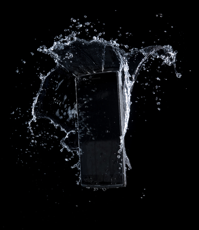 Smartphone with splashing of water or explosion flying in the air isolated on blackの写真素材
