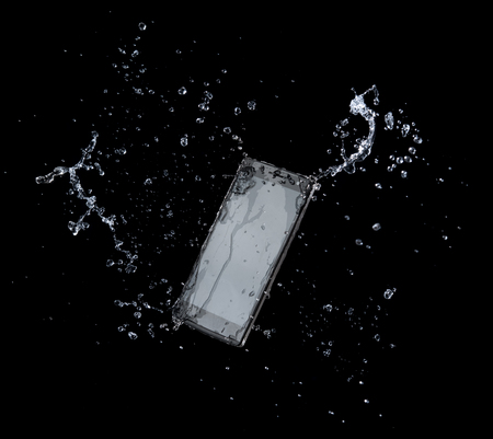 Smartphone with splashing of water or explosion flying in the air isolated on blackの写真素材