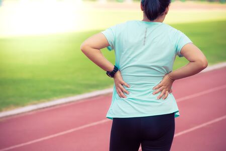 Female runner painful lower back pain injury and pain on running track,Injury from workout concept