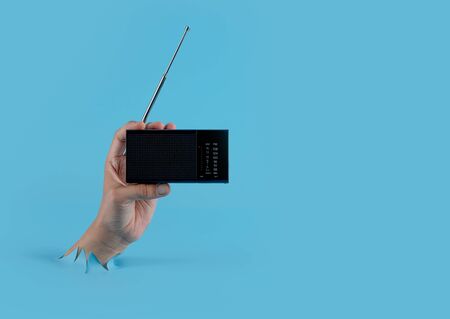 Hand holding a radio through the torn blue plastic backgroundの写真素材
