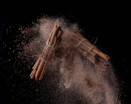 Cinnamon sticks with powder splash or explosion flying in the air isolated on black backgroundの写真素材