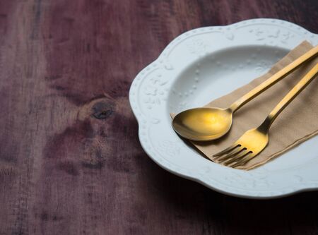 Empty plate with brass spoon and fork on wooden backgroundの写真素材
