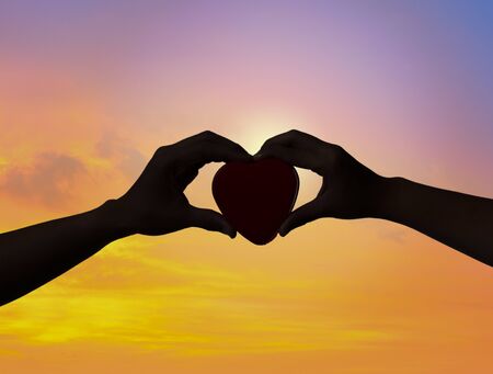 Silhouette of female and man's hands with red heart at sunsetの写真素材