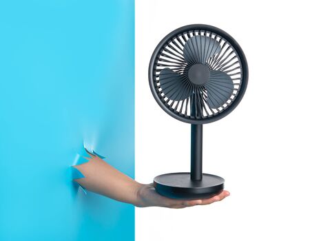 Hand holding Electric table fan through the torn blue plastic isolated on white backgroundの写真素材