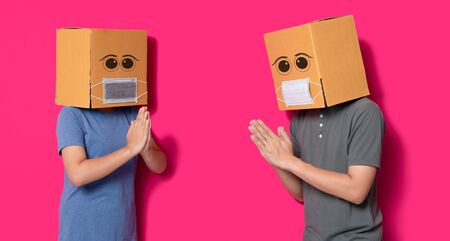 Man and woman wearing cardboard box with mask to protect from COVID 19 virus,Thai Wai, Social...