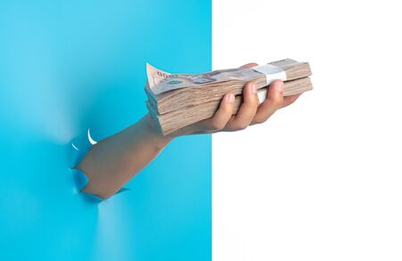 Hand holding pack of money through the torn blue plastic isolated on white backgroundの写真素材