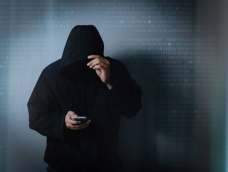 Internet crime concept,Hooded hacker using smartphone in dark roomの写真素材