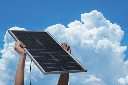Hand holding a solar panel on blue sky background,alternative clean green energy conceptの写真素材