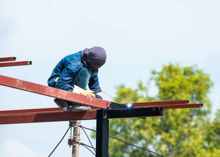 a man works with a welding machine and metal on the roofの写真素材