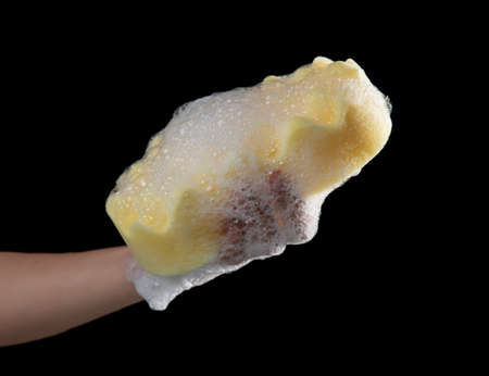Cleaning the car,Hand holding a yellow sponge wet with foam isolated on a black backgroundの写真素材