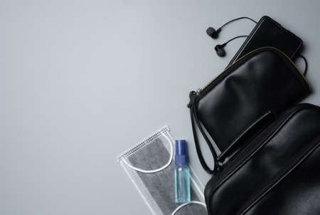 COVID-19 protection and new normal lifestyle concept,black bag with a phone, a mask and an alcohol spray bottle on gray background with copy spaceの写真素材