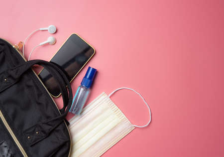 COVID-19 protection and new normal lifestyle concept,black bag with a phone, a mask and an alcohol spray bottle on gray background with copy spaceの写真素材