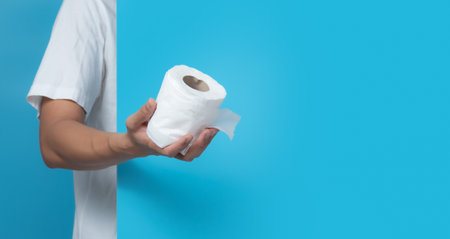 Male hand holding white toilet paper roll on blue background,copy space for textの写真素材