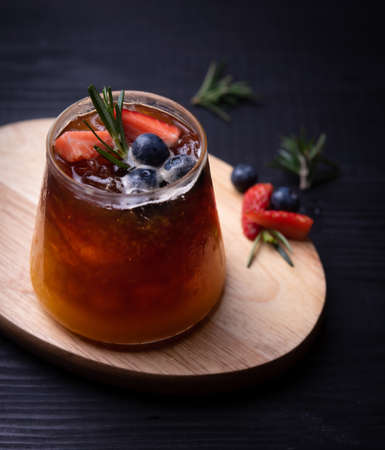glass of iced americano black coffee and layer of orange with rosemary,blueberries,orange and strawberry on woodの写真素材