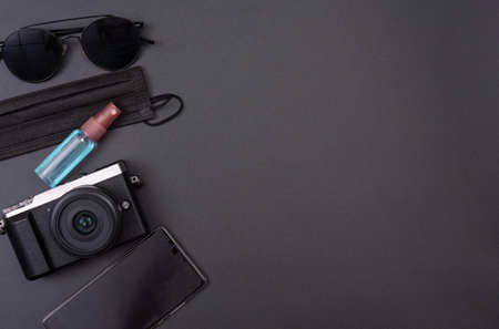 Travel concept:Top view photo of sunglasses compass camera with masks and sanitizer on dark...
