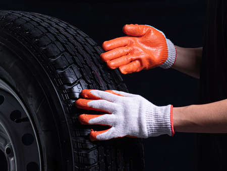 Auto mechanic checking a car tire on a black backgroundの写真素材