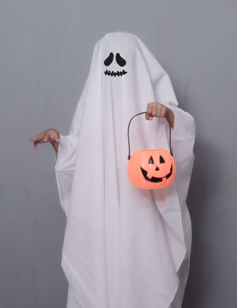 Halloween Concept,Cute little kid in ghost costume with halloween pumpkin candy jar doing trick or...