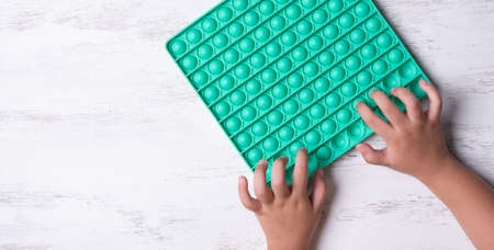 Child with green poppit game. Close up bunner shot of kid hands playing with green  fidget toyの写真素材