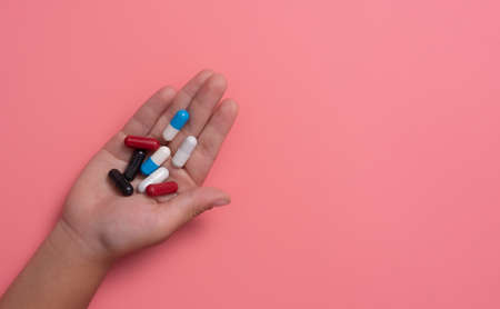 kid's hands with colorful pharmaceutical medicine capsules on pink backgroundの写真素材