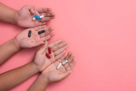 kid's hands with colorful pharmaceutical medicine capsules on pink backgroundの写真素材