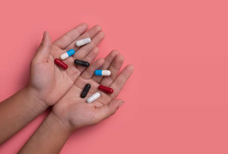kid's hands with colorful pharmaceutical medicine capsules on pink backgroundの写真素材