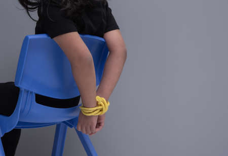 Child's hands tied with rope sitting chair kidnapping conceptの写真素材