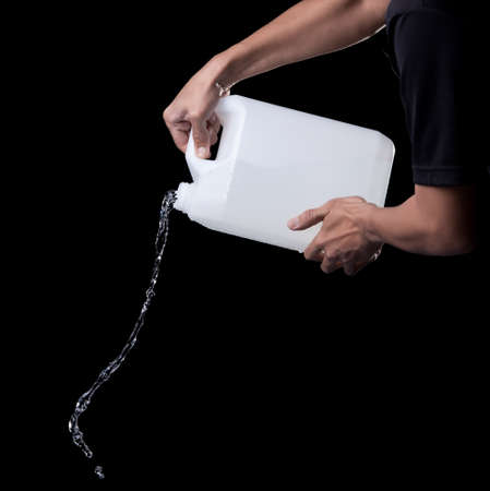 Hand pouring water from plastic container on black background.の写真素材