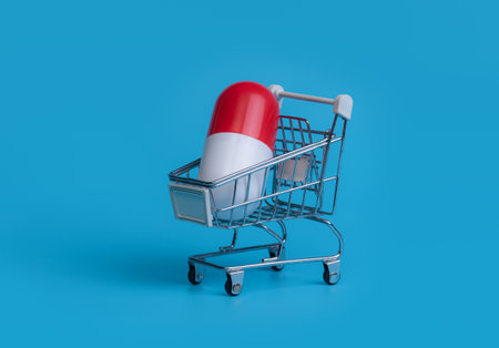 Big capsule in shopping cart on blue background. Shopping trolley with pill and capsule. Pharmacy medicine concept.の写真素材
