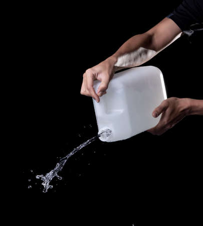 Hand pouring water from plastic container on black background.の写真素材